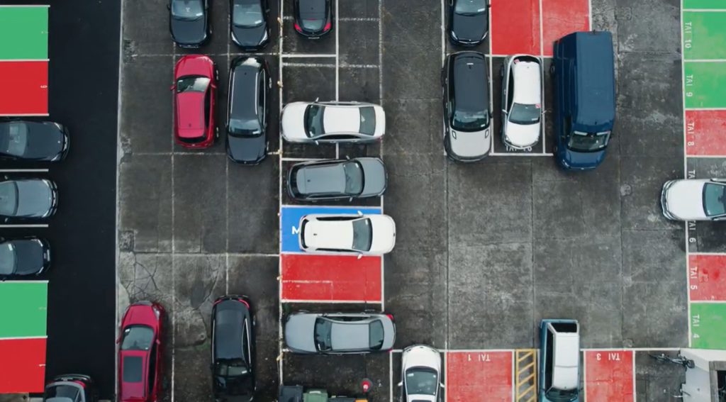 Aerial view of LK Shields' car park - spaces that are free are shown in green, and spaces already booked shown in red. The space booked by an employee is booked in blue, and they are reversing their car into their booked space.